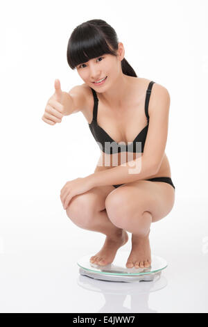 Schöne chinesische Frau wiegen sich auf einer Skala und begeistert mit den Ergebnissen, die auf einem weißen Hintergrund isoliert Stockfoto