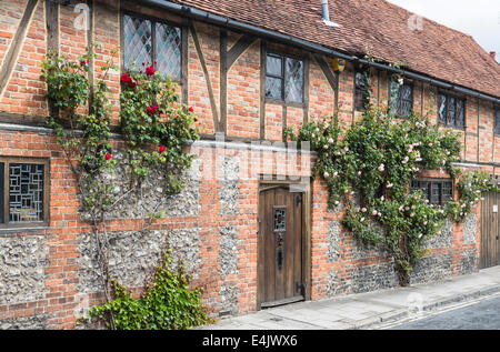 Aus rote Backstein gebaut Fachwerkhaus terrassenförmig angelegten Häuser in Henley-on-Thames, Oxfordshire, Vereinigtes Königreich, mit roten und rosa Rosen rund um das Fenster Stockfoto