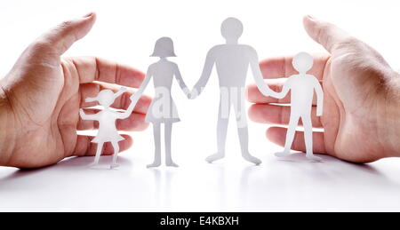 Pappfiguren der Familie auf einem weißen Hintergrund. Das Symbol der Einheit und des Glücks. Händen umarmen sanft die Familie. Stockfoto