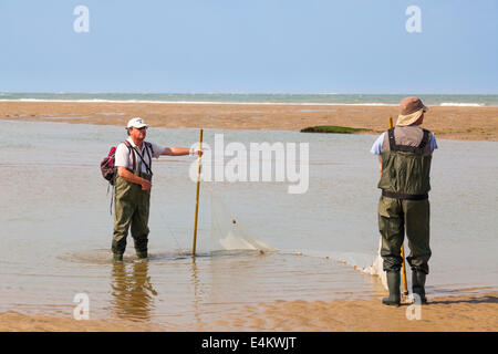 Zwei Fischer, die Schleppnetzfischerei für Fisch am Strand mit einem Netz in ein in einem Pool von der zurückweichenden Flut verlassen. Stockfoto