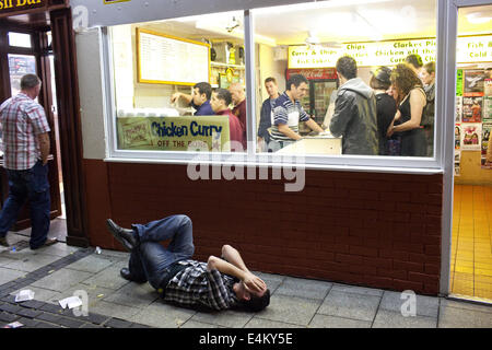 Ein junger Mann liegt auf dem Bürgersteig vor einem Pommesbude auf ein Wochenende Nacht in Cardiff, Wales, UK Stockfoto