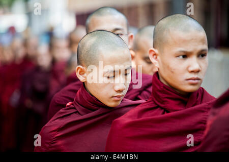 Junge buddhistische Mönche warten in der Schlange für Lebensmittel im Rahmen einer Almosen Zeremonie im Maha Aung Mye Bonzan Kloster in Mandalay, Myanmar. Stockfoto