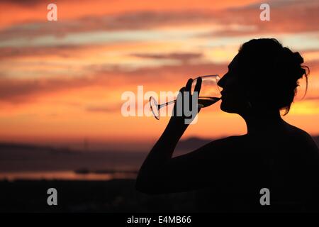 Schöne Silhouette einer Frau trinken ein Glas Wein vor einem Sonnenuntergang Stockfoto