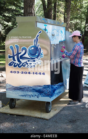 Frau füllt wiederverwendbare Wasserflasche mit Trinkwasser aus H2O Buggy (mobile Wasserstation) im Stadtpark Stockfoto
