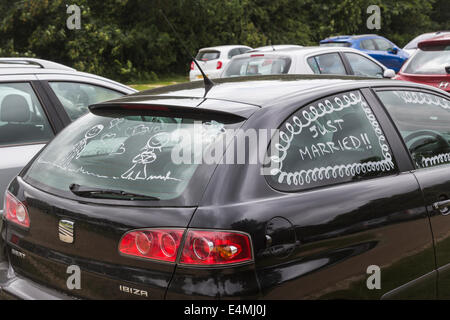 Hochzeitsreisende schwarze Auto lackiert mit "Just Married!" am Seitenfenster und Figuren der Braut und des Bräutigams an Heckscheibe Stockfoto