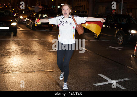 Wiesbaden, Deutschland 14. Juli 2014. Deutschland gewinnt das FIFA WM 2014. Menschen in ihren Autos und auf der Straße, jubeln und feiern in der Innenstadt von Wiesbaden nach Deutschlands Sieg über Argentinien im Endspiel. Eine junge Frau mit einer deutschen Flagge Tänze auf der Straße. Bewegungsunschärfe. Bildnachweis: Oliver Kessler/Alamy Live-Nachrichten Stockfoto