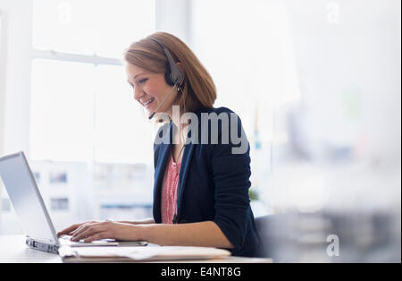 Junge Büroangestellte am Kopfhörer sprechen und schreiben Stockfoto