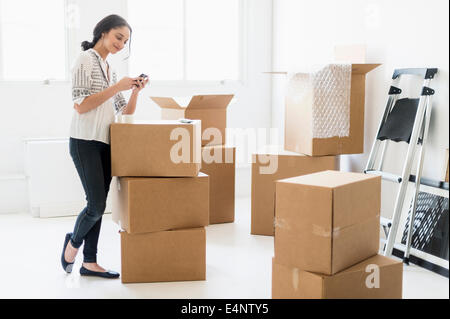 Junge Frau, die unter den Boxen im neuen Zuhause und mit Handy Stockfoto