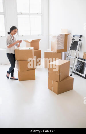 Junge Frau, die unter den Boxen im neuen Zuhause und mit Handy Stockfoto