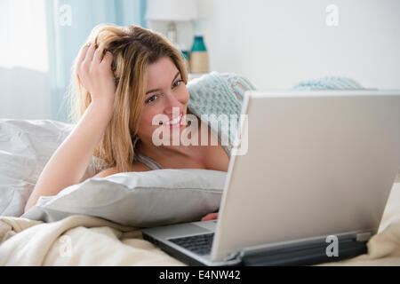 Junge Frau im Bett liegend und mit laptop Stockfoto