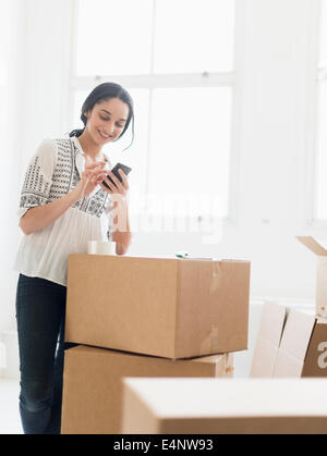 Junge Frau, die unter den Boxen im neuen Zuhause und mit Handy Stockfoto