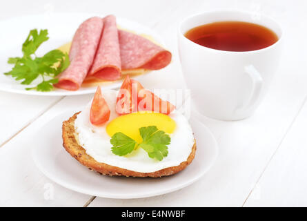 Frühstück - Sandwich mit Spiegelei, Tomatenscheiben und Tee auf Holztisch Stockfoto