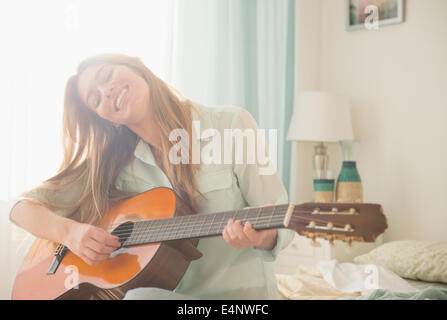 Junge Frau, die Akustik-Gitarre auf Bett Stockfoto