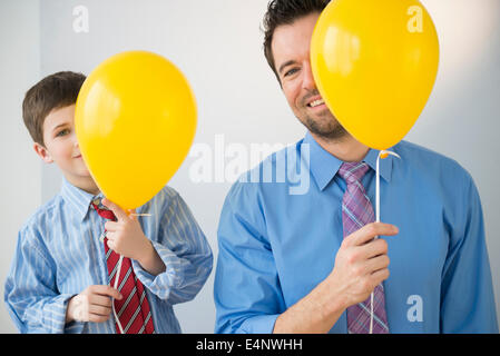 Vater und Sohn (8-9) spähen hinter gelben Ballons Stockfoto