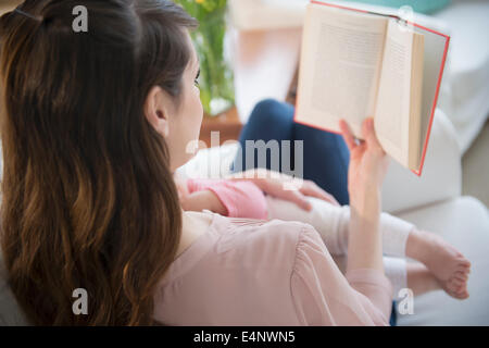 Junge Frau liest Buch und Holding-Tochter (6-11 Monate) Stockfoto