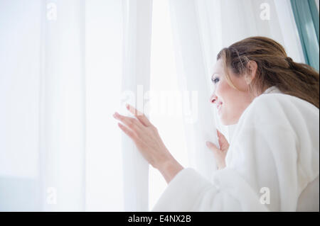 Frau trägt Bademantel Blick durch Fenster Stockfoto