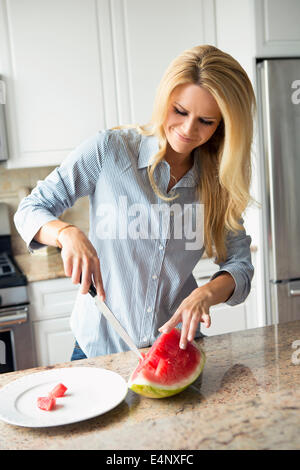 Blonde Hausfrau schneiden Wassermelone Stockfoto