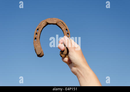 weibliche Hand halten Vintage metallischen rostigen Hufeisen auf blauen Himmelshintergrund Stockfoto