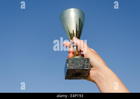 weibliche Hand halten Award metallischen Cup am blauen Himmelshintergrund Stockfoto