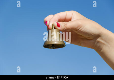 Frau Hand mit roten Nägeln schütteln kleine eiserne Glocke und jingle Sounds auf der Hintergrund des blauen Himmels. Stockfoto
