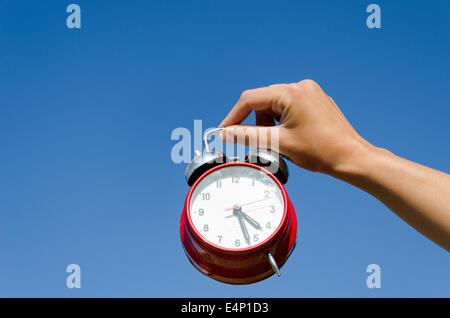 weibliche Hand halten rot Chrom glänzend Wecker auf blauen Himmelshintergrund Stockfoto