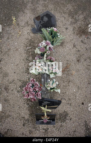 Detail eine Gedenkstätte und künstliche Blumen auf einem verwilderten Grab in einem ländlichen französischen Dorf in Indre-et-Loire. Stockfoto