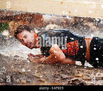 Ein Mann kriecht durch die While besprüht mit einem Feuerwehrschlauch auf dem Whistler Vancouver Tough-Mudder-Event. Stockfoto