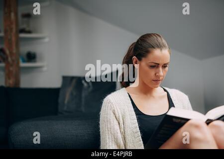 Bild der jungen Frau ein Buch zu lesen. Kaukasische weiblich zu Hause sitzen durch eine Couch mit einem Roman. Stockfoto