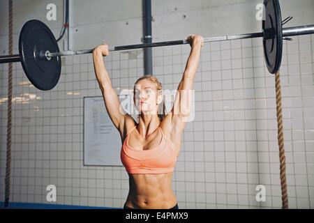 Schöne starke junge Frau mit Langhantel und Gewicht Platten Overhead. Passen Sie die junge Sportlerin, schwere Gewichte zu heben. Kaukasische Stockfoto