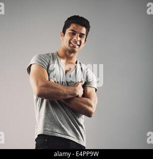 Porträt von intelligenten jungen muskulöser Mann posiert vor grauem Hintergrund. Glückliche junge hispanic Männermodel stehend mit seinen Armen cros