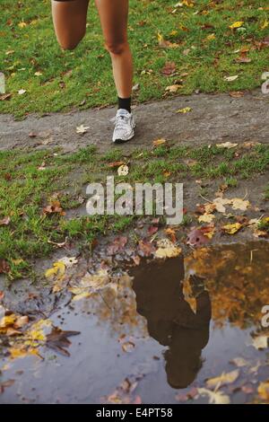 Reflexion der junge Frau in eine Wasserpfütze im Park. Geringen Teil der Fitness, die weibliche Beine dehnen zu tun im Freien ausüben Stockfoto