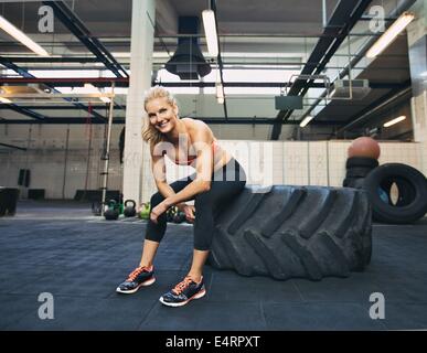 Frau auf Reifen lächelnd in die Kamera im Fitnessstudio. CrossFit Sportlerin Rast nach dem Training. Stockfoto