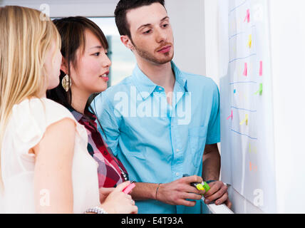 Nahaufnahme von drei jungen Geschäftsleuten treffen, stehen und blickte am Whiteboard im Büro, Deutschland Stockfoto