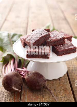 Nahaufnahme von Rüben Gemüse neben weißen Kuchen Stand halten Rüben Brownies auf hölzernen Hintergrund, Studio gedreht Stockfoto
