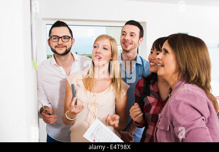 Reife Geschäftsfrau Treffen mit einer Gruppe von jungen Geschäftsleuten, mit Blick auf weiße Tafel und lächelnd, Deutschland Stockfoto