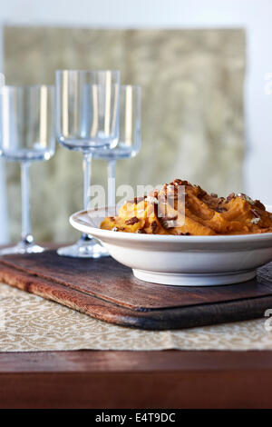 Große Schüssel von Sweet Kartoffelpüree garniert mit Pekannüssen vor leere Gläser Wein Stockfoto