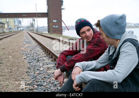 Zwei Jungs im Teenageralter auf Eisenbahnschienen beisammen sitzen, in der Nähe von Hafen, Deutschland Stockfoto