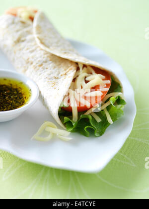 Vegetarische weichen Taco wickeln mit Salat, Tomate und Monterey Jack Käse auf einem weißen Teller mit Kräutern Olivenöl auf der Seite. Stockfoto