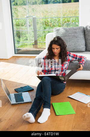 Draufsicht der Teenager-Mädchen auf Boden neben Sofa sitzen, Lesen von Binder und verwenden von Laptop-Computer, Deutschland Stockfoto