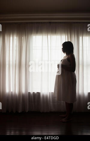 Silhouette der schwangeren Frau schaut aus Fenster Stockfoto