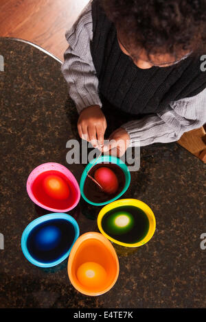 Obenliegende Ansicht von Boy mit Färbung Cups zu färben Ostereier auf Granit Küchenarbeitsplatte Stockfoto