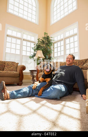 Porträt von reifer Mann mit seinem Haustier Rottweiler im Wohnzimmer Stockfoto