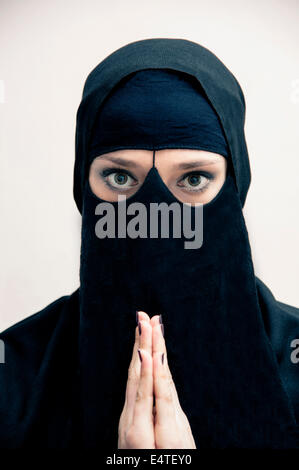 Porträt der jungen Frau in schwarz, islamischen Hijab und Muslim Kleid, mit Händen beten, Blick in die Kamera, auf weißem Hintergrund Stockfoto