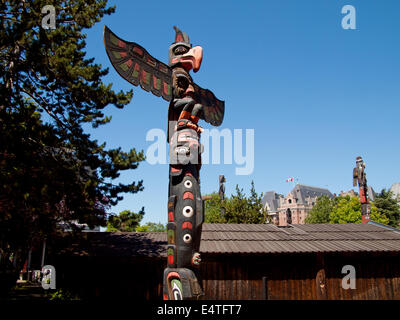 Ein Kwakwa̱ka̱'Wakw Totempfahl im Thunderbird Park in Victoria, British Columbia, Kanada. Fairmont Empress Hotel im Hintergrund. Stockfoto