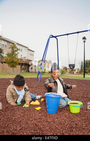 Brüder spielen mit Rubber Mulch und Eimer im Spielplatz, Maryland, USA Stockfoto