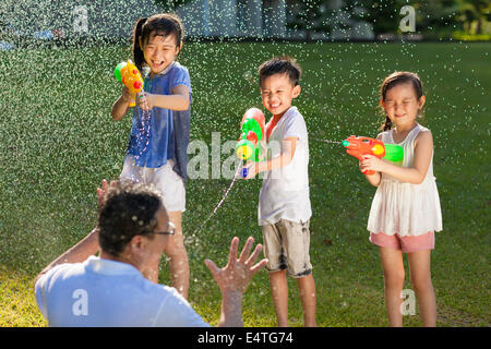 kleine Jungs mit Wasserpistolen zu ihrem Vater zu sprühen Stockfoto