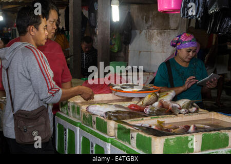 Bali, Indonesien.  Jimbaran Fischmarkt.  Frau Preisberechnung von Fisch für zwei Käufer. Stockfoto