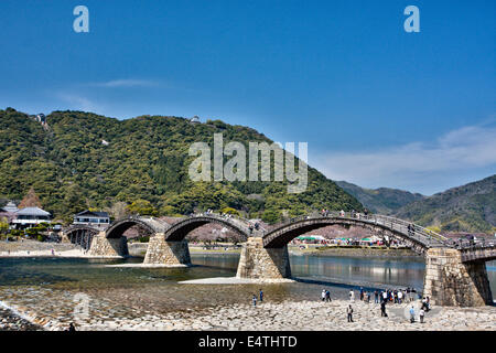 Der historische Holzbogen Kintai Brücke über den Nishiki Fluss bei Iwakuni mit den Bergen hinter und die Burg am Horizont. Blauer Himmel. Stockfoto