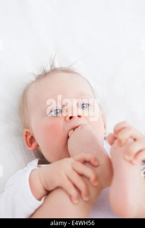 Niedliche Baby platzieren ihren Fuß auf den Mund Stockfoto