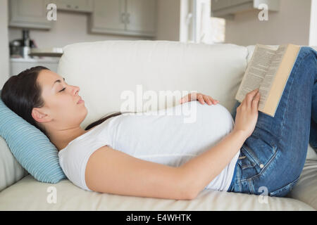 Junge schwangere Frau liest auf sofa Stockfoto